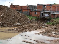 Fotografia de esgoto a céu aberto no terreno atrás de diversas casas.